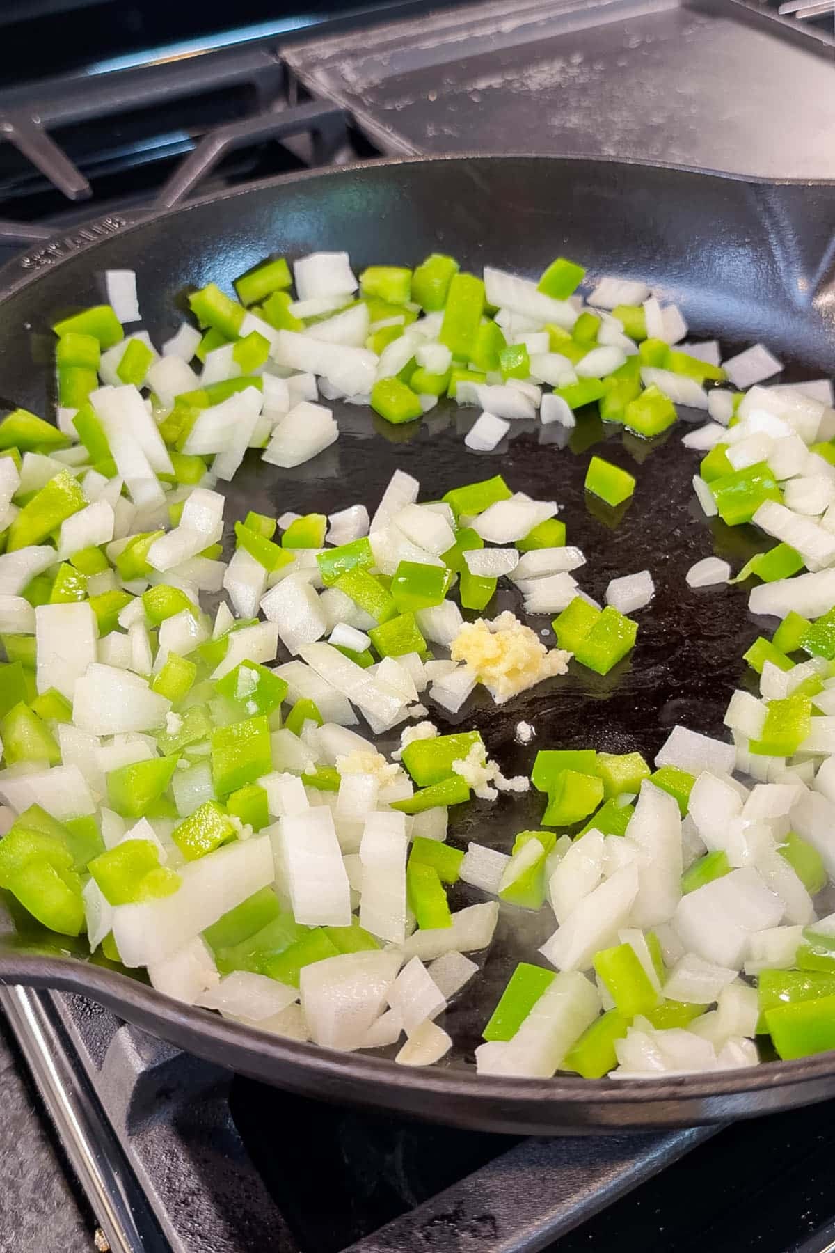 Diced yellow onion, green bell pepper, and minced garlic in a cast-iron skillet for Green Chile Chicken Enchilada Skillet.