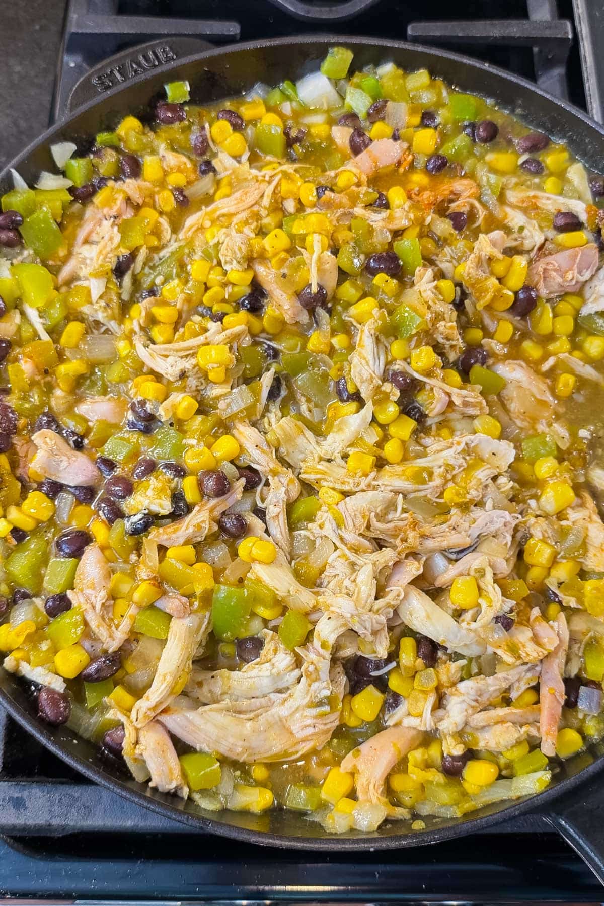 Simmered green chile chicken mixture with beans and corn in a cast-iron skillet for Green Chile Chicken Enchilada Skillet.