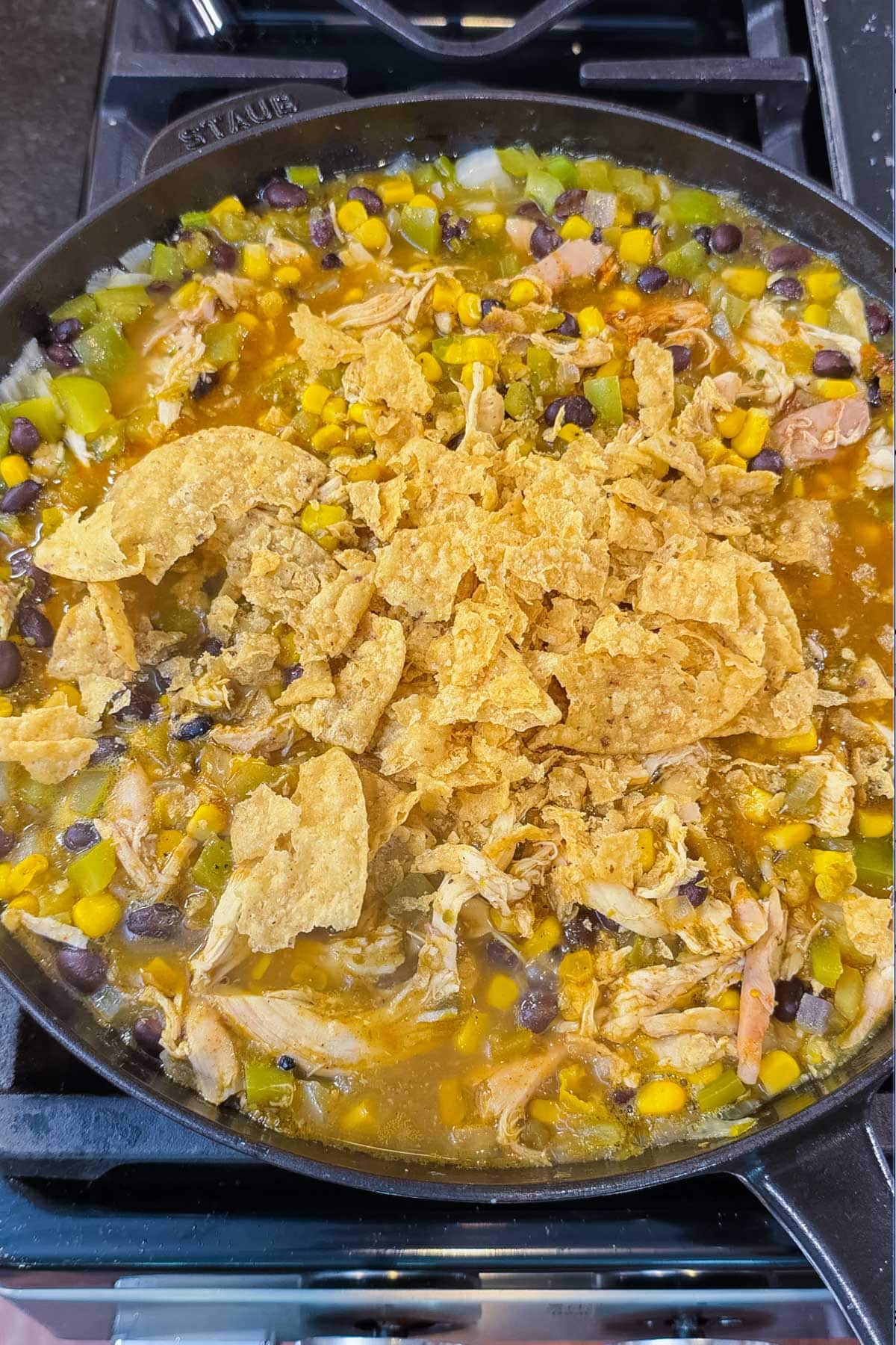 Crushed tortilla chip pieces folded into the green chile chicken mixture in a cast-iron skillet right before the cheese topping for Green Chile Chicken Enchilada Skillet.