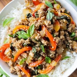 A Thai Basil Ground Turkey stir-fry recipe is in a white dinner bowl with bell peppers and fresh basil.