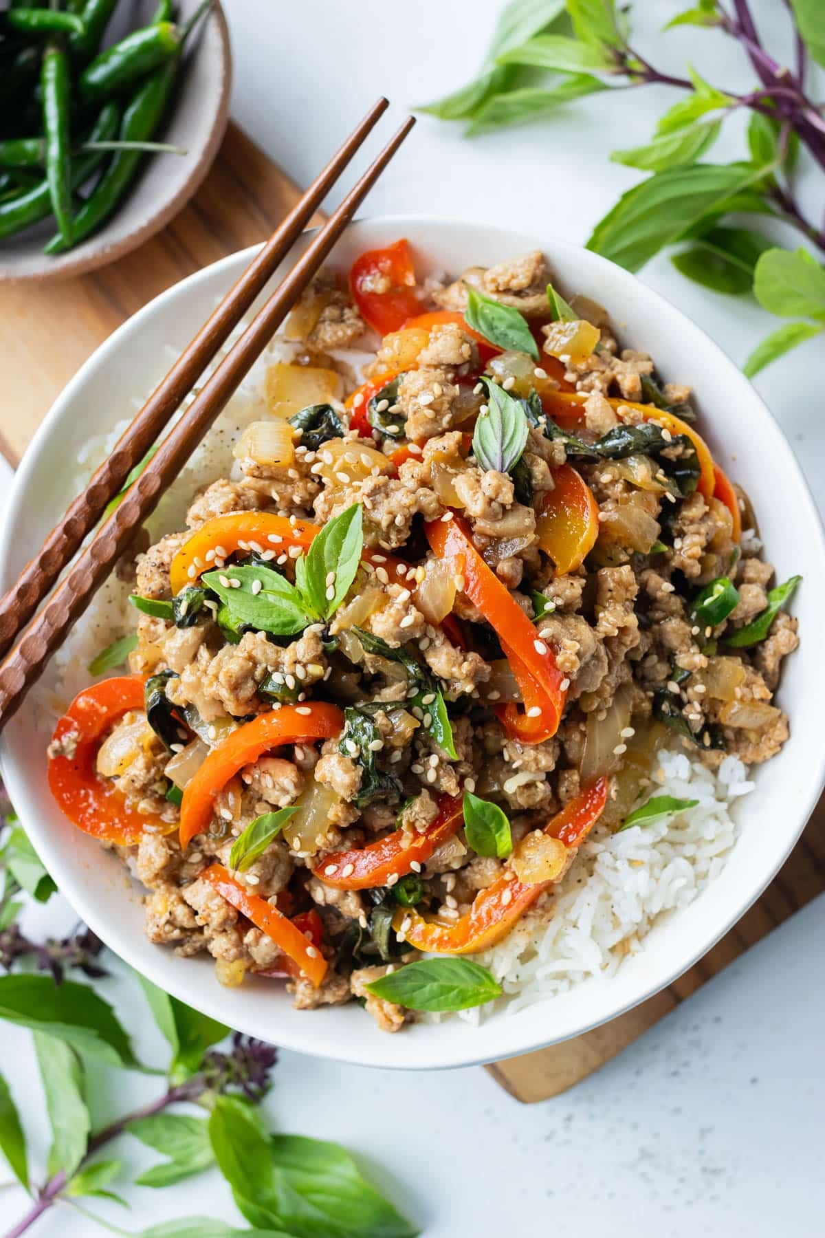 Thai Basil Ground Turkey Stir-Fry is served in a white bowl over rice with chopsticks and fresh basil.