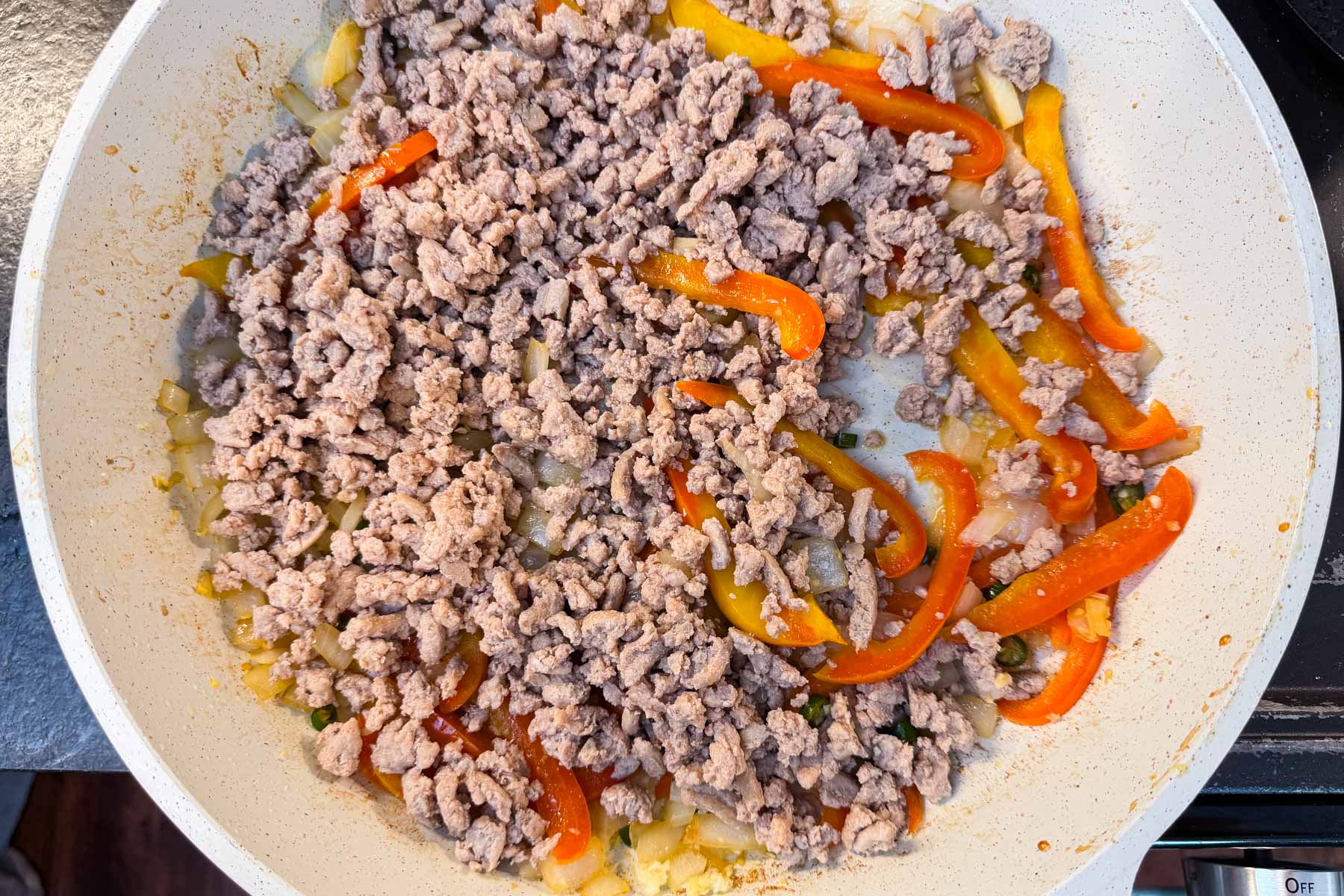 Ground turkey stirred back into the skillet with cooked bell peppers and onions