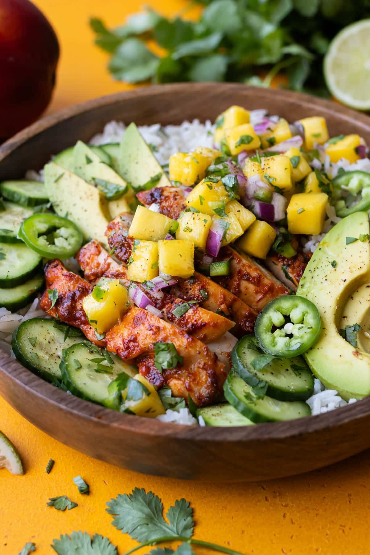 A mango chipotle chicken rice bowl is served with salsa, cucumbers, and avocado for an easy summer dinner.