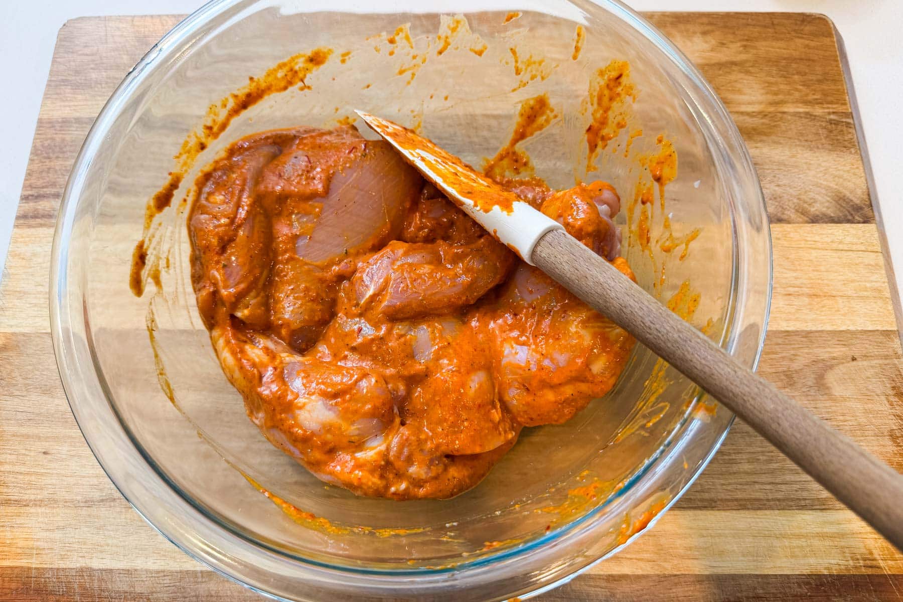 Chicken thighs tossed with chipotle mango marinade in a glass bowl with a wooden spatula.