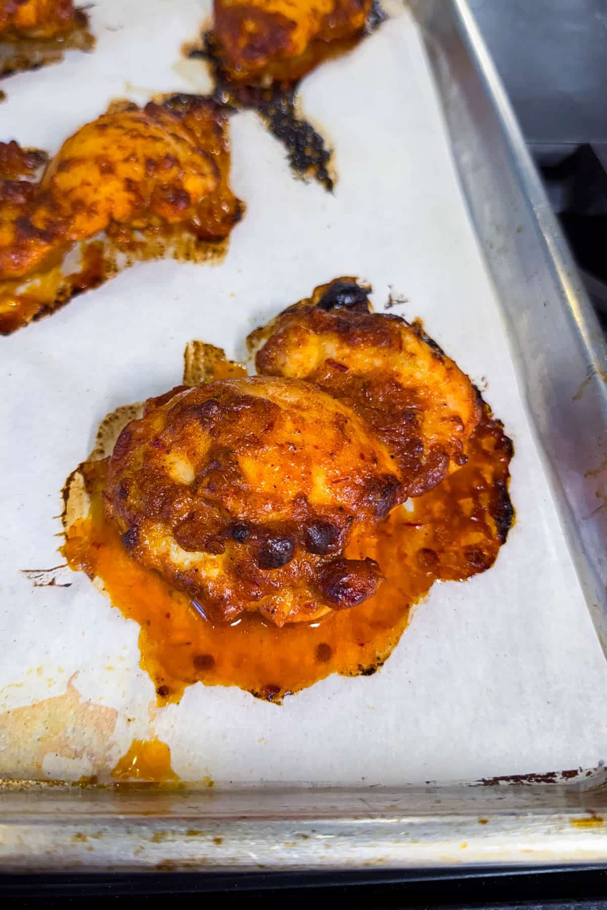 A baked chipotle mango chicken thigh on a parchment-lined sheet pan with caramelized edges.