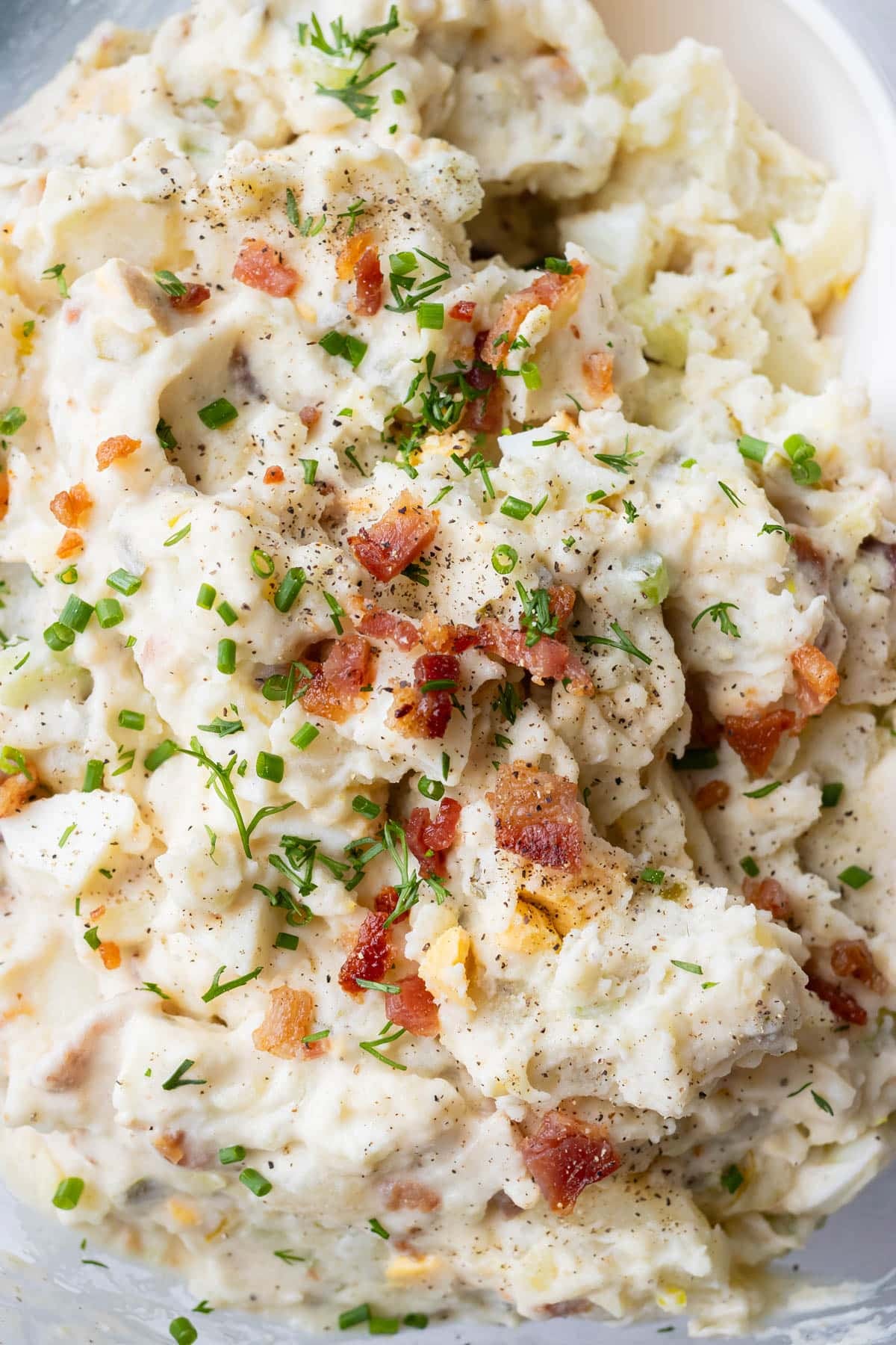 A bowl of classic potato salad with bacon, eggs, and chives.