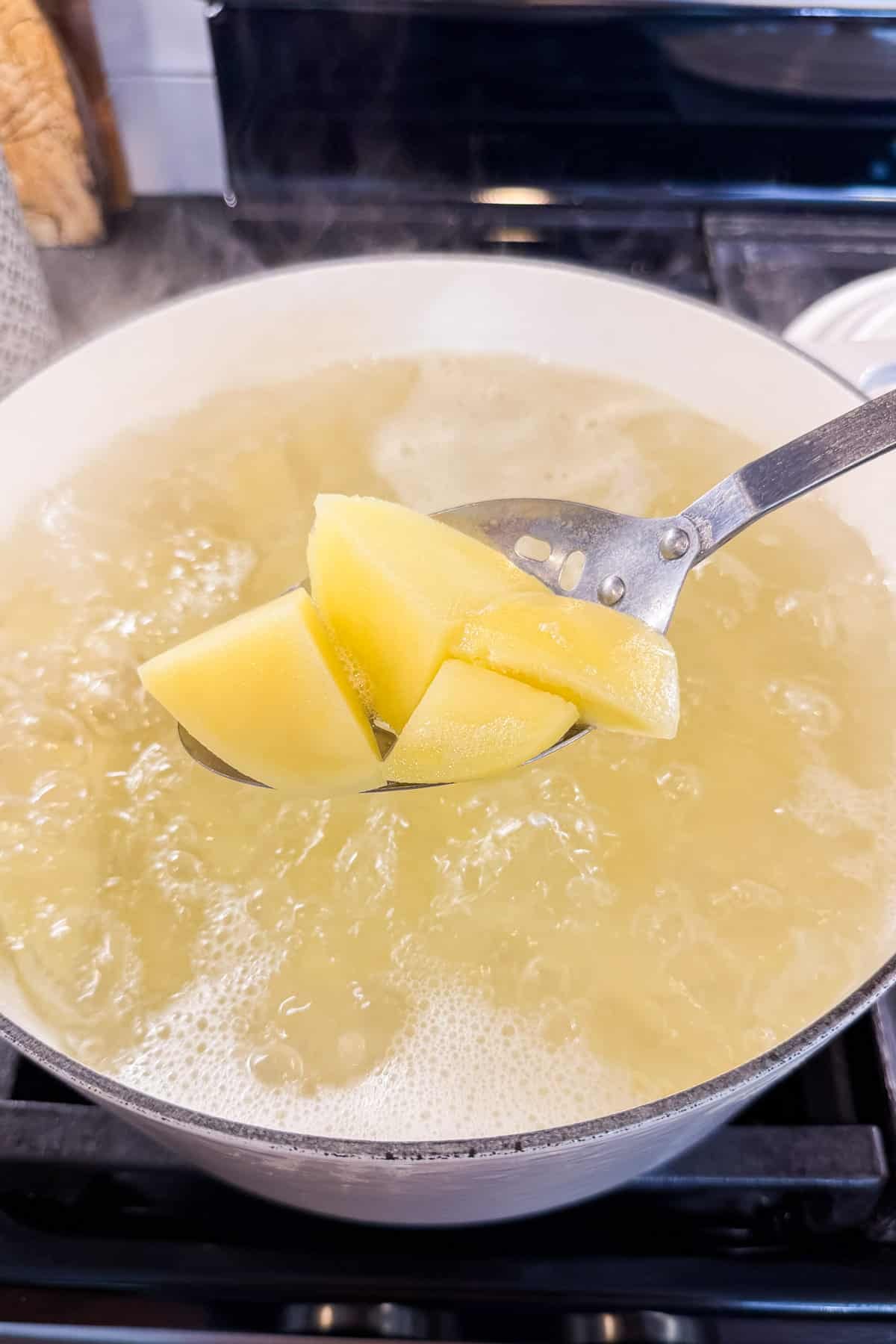 Cubed potatoes lifted from boiling water with a slotted spoon.