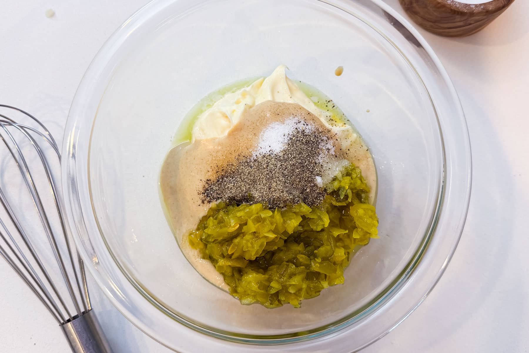 Mayonnaise, Dijon mustard, dill pickle relish, and seasonings in a glass bowl ready to be whisked into a creamy potato salad dressing.