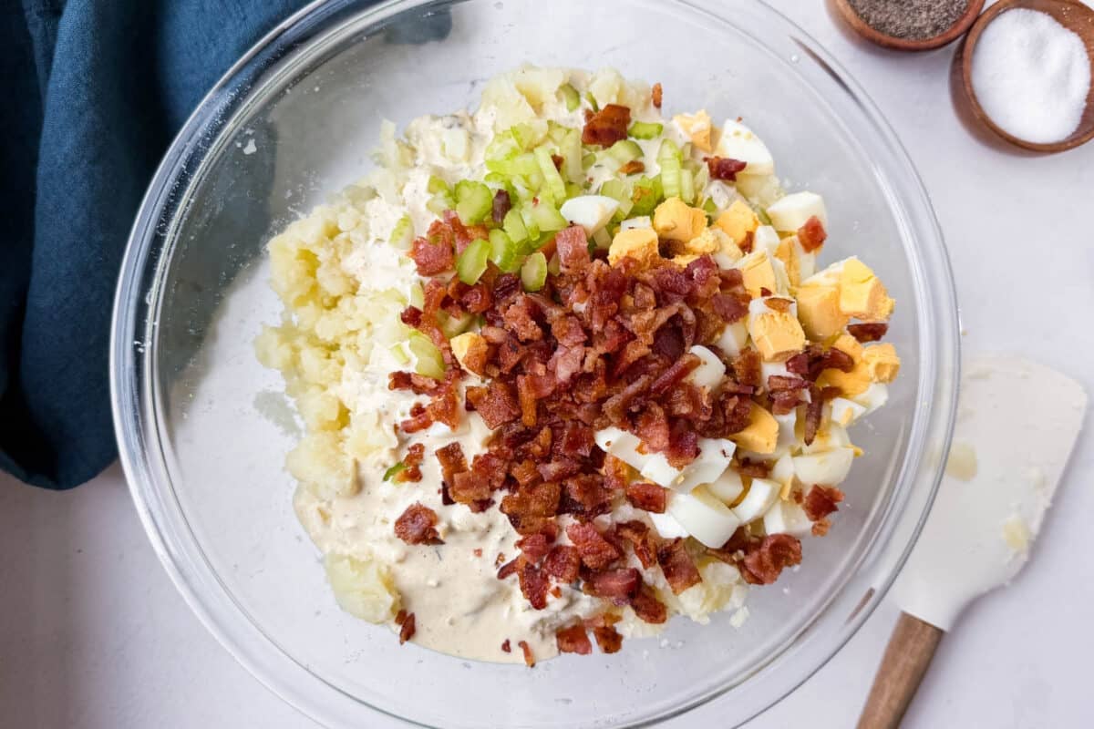 Smashed potatoes topped with crumbled bacon and chopped hard-boiled eggs ready to be folded together.