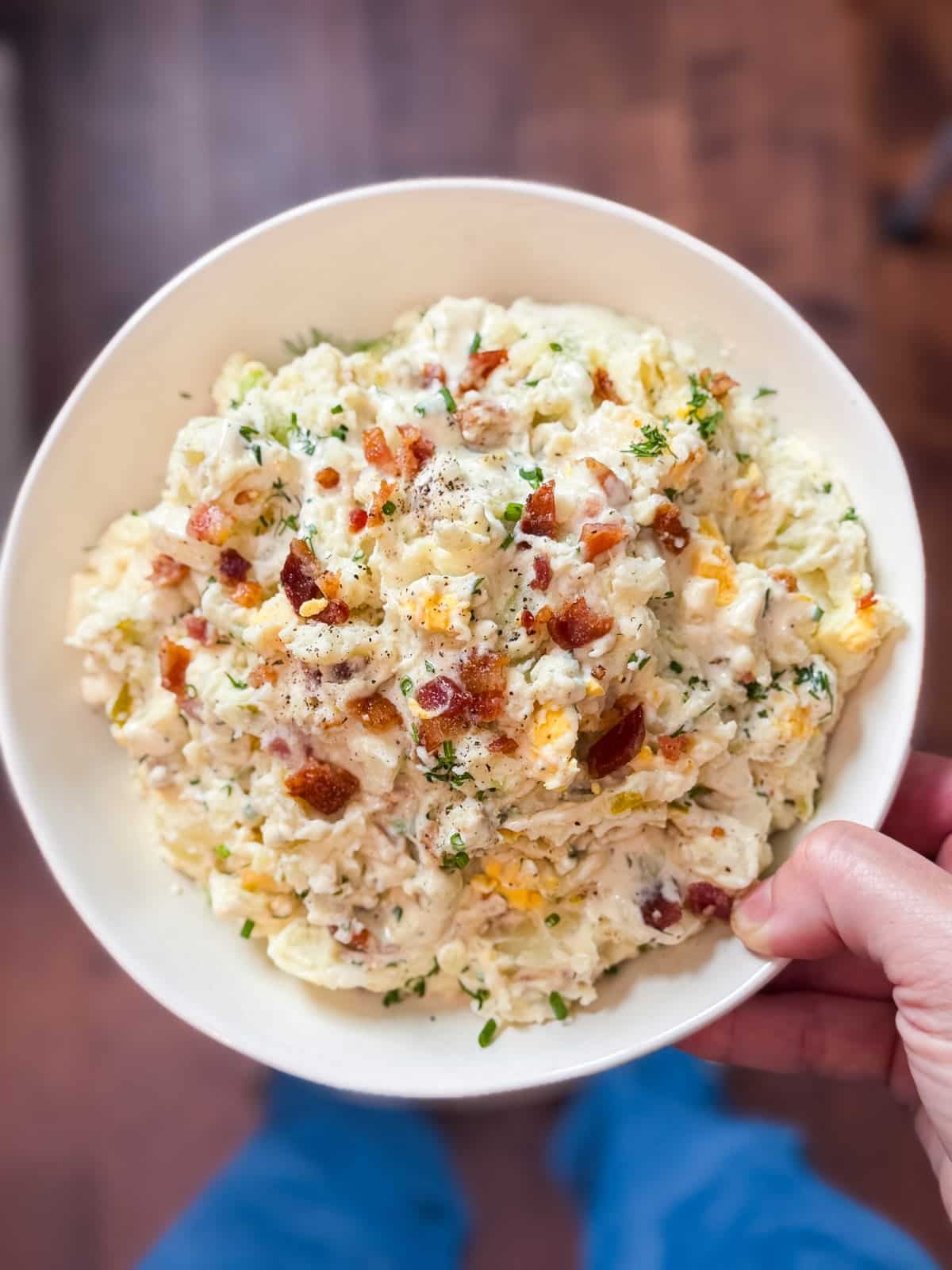 Finished classic potato salad with bacon, eggs, and chives in a white serving bowl.