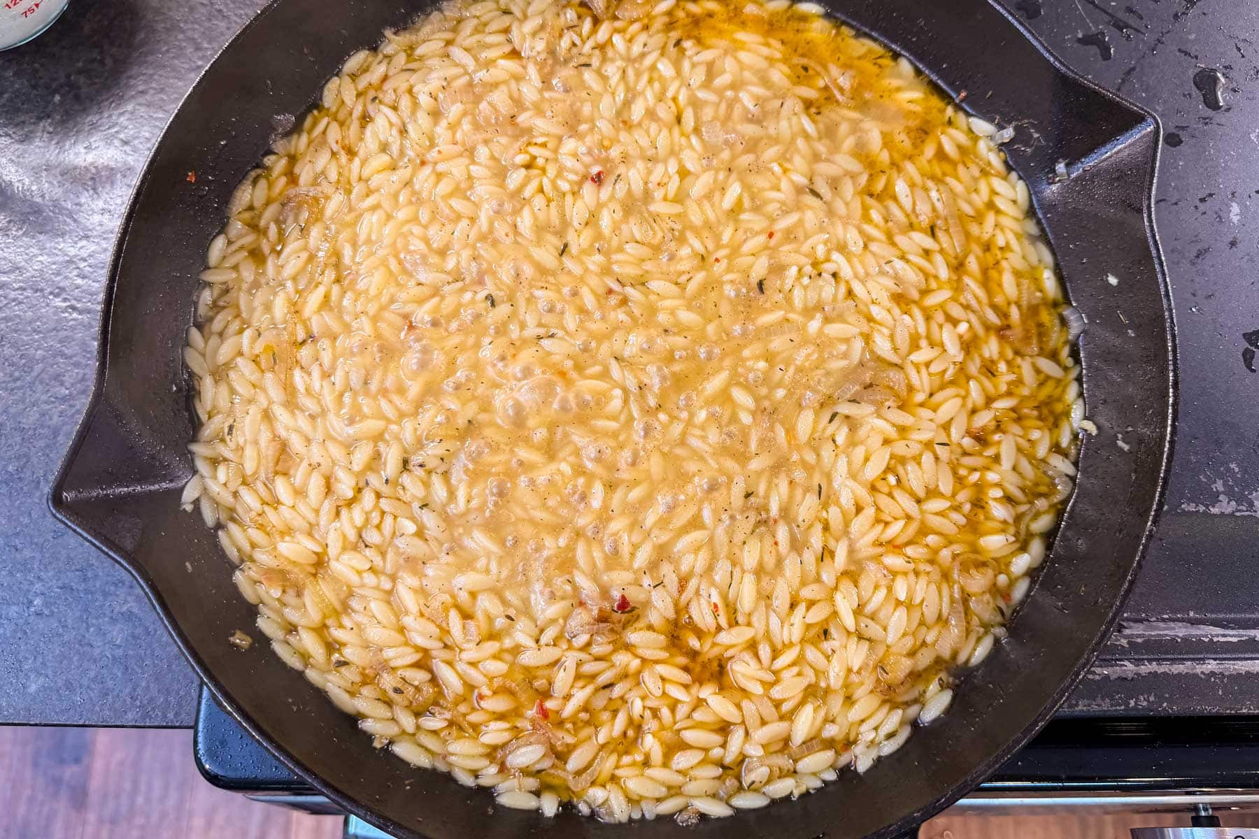 Cooked tender orzo in a cast iron skillet after absorbing the broth and cream.
