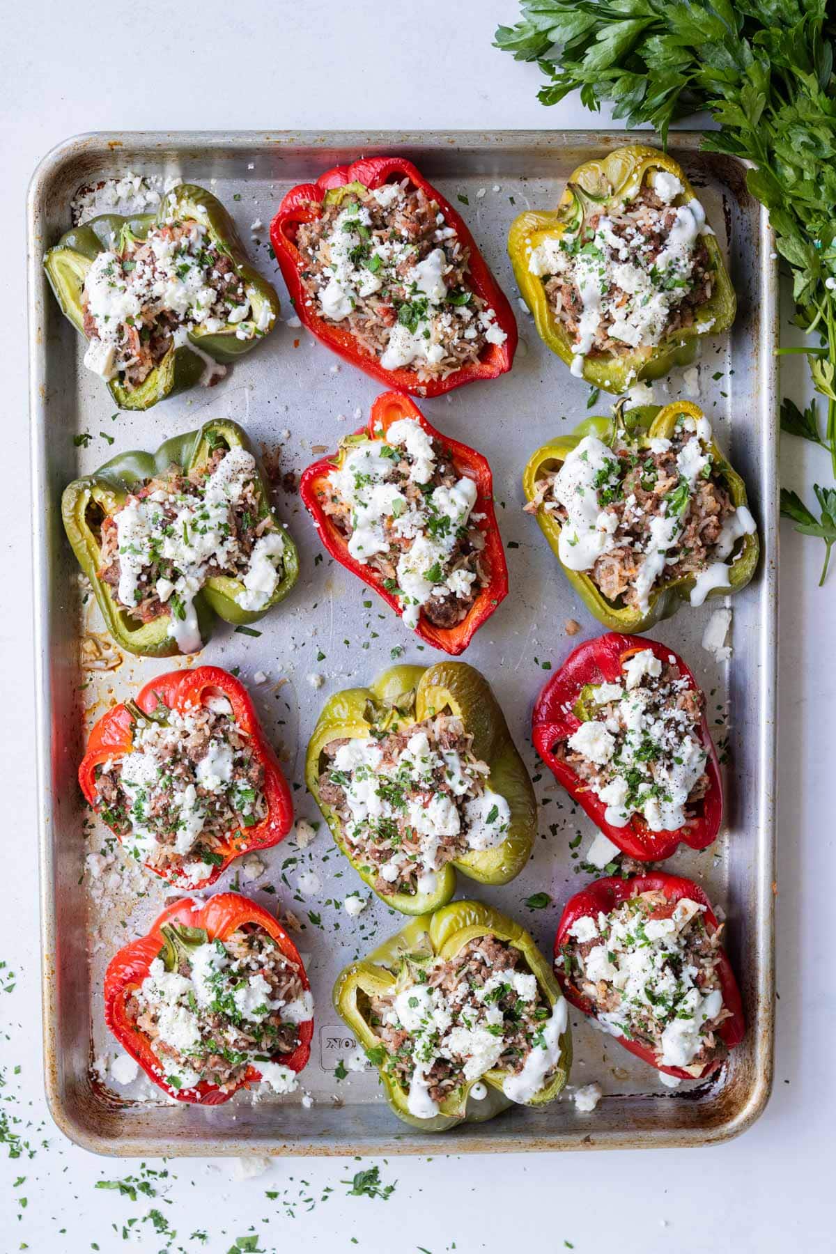 Stuffed peppers are on a sheet pan full of a Greek-inspired ground beef and rice filling.