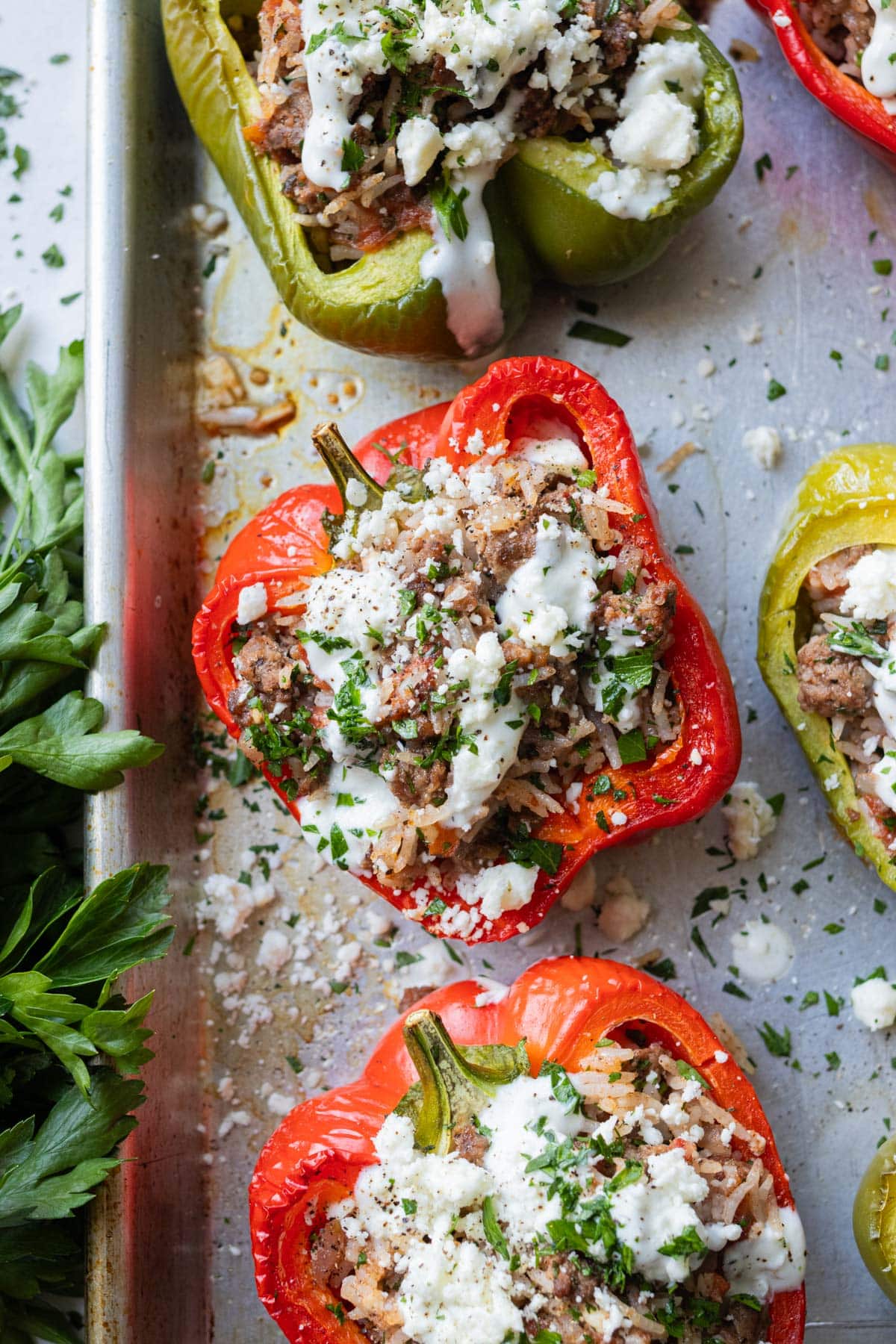 Red and green Greek Stuffed Bell Peppers with a beef and rice filling are on a sheet pan after baking in the oven.
