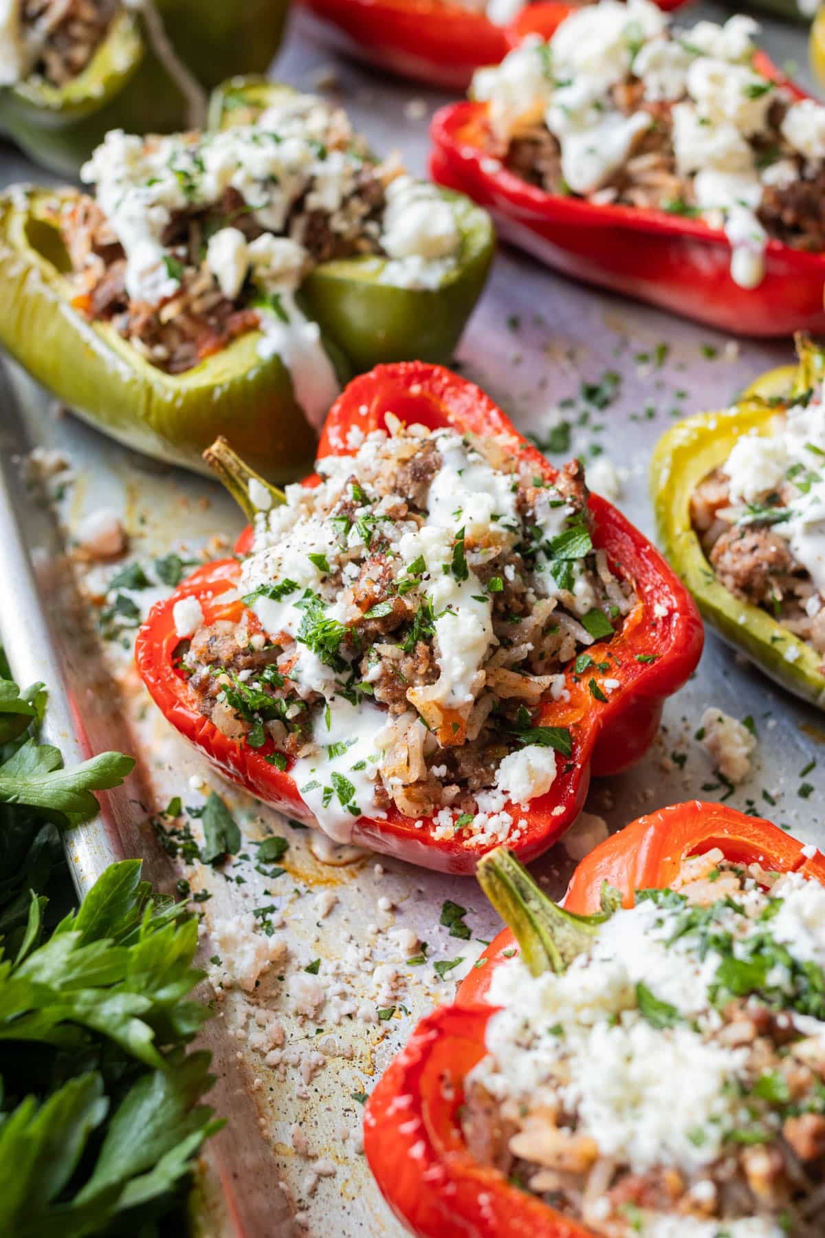Greek stuffed peppers with a beef and rice filling, feta cheese, and tzatziki sauce on a baking sheet.