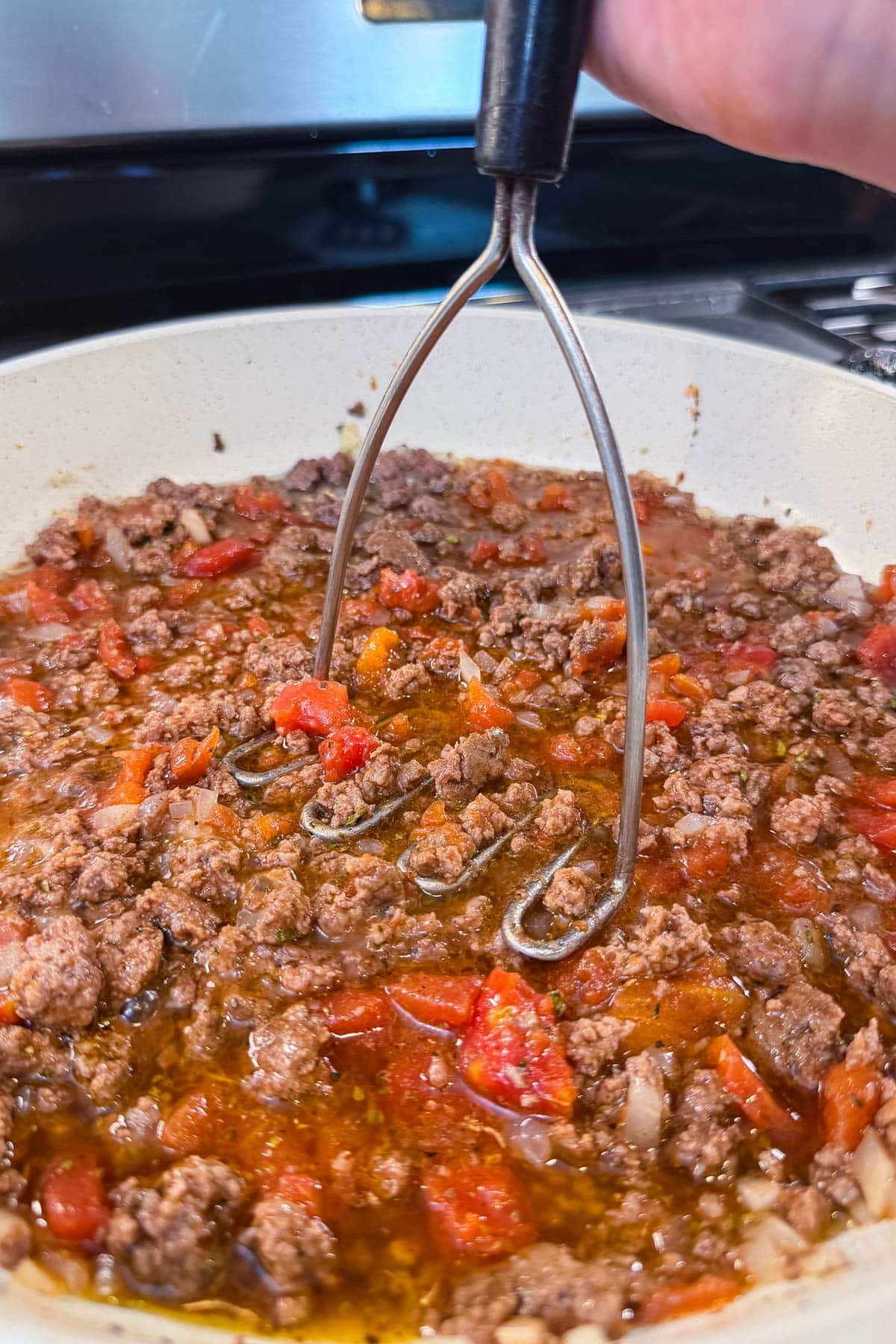 Ground beef, tomatoes, and greek spices are cooked in a skillet.