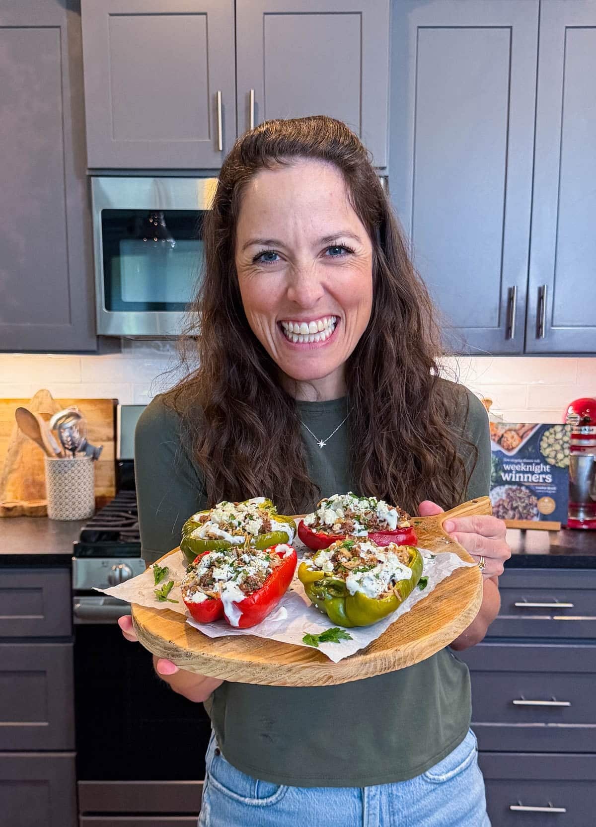 London Lea holding a tray full of Greek Stuffed Bell Peppers in her Austin, Texas kitchen.