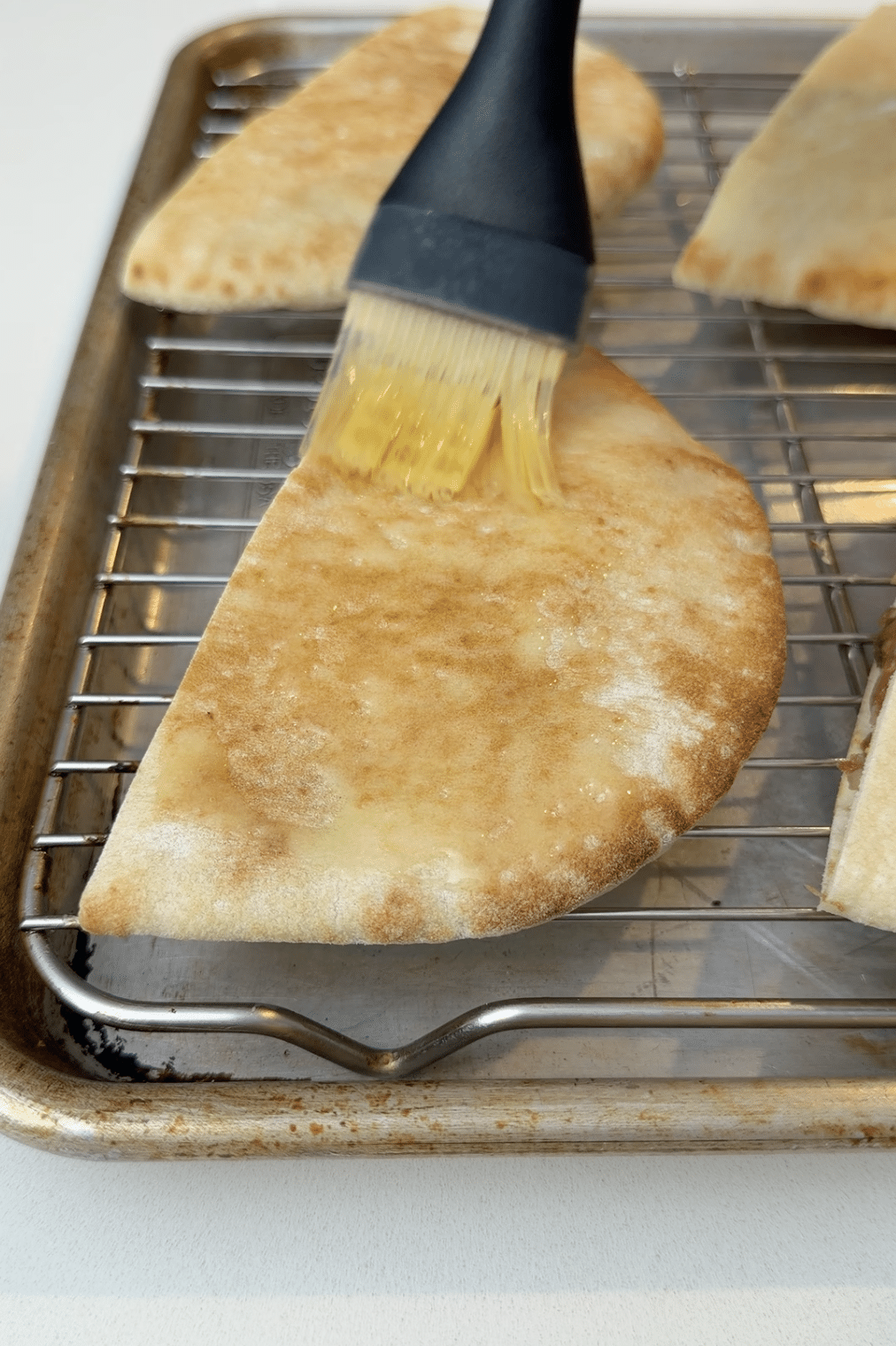 Brushing garlic butter onto meat stuffed pitas.