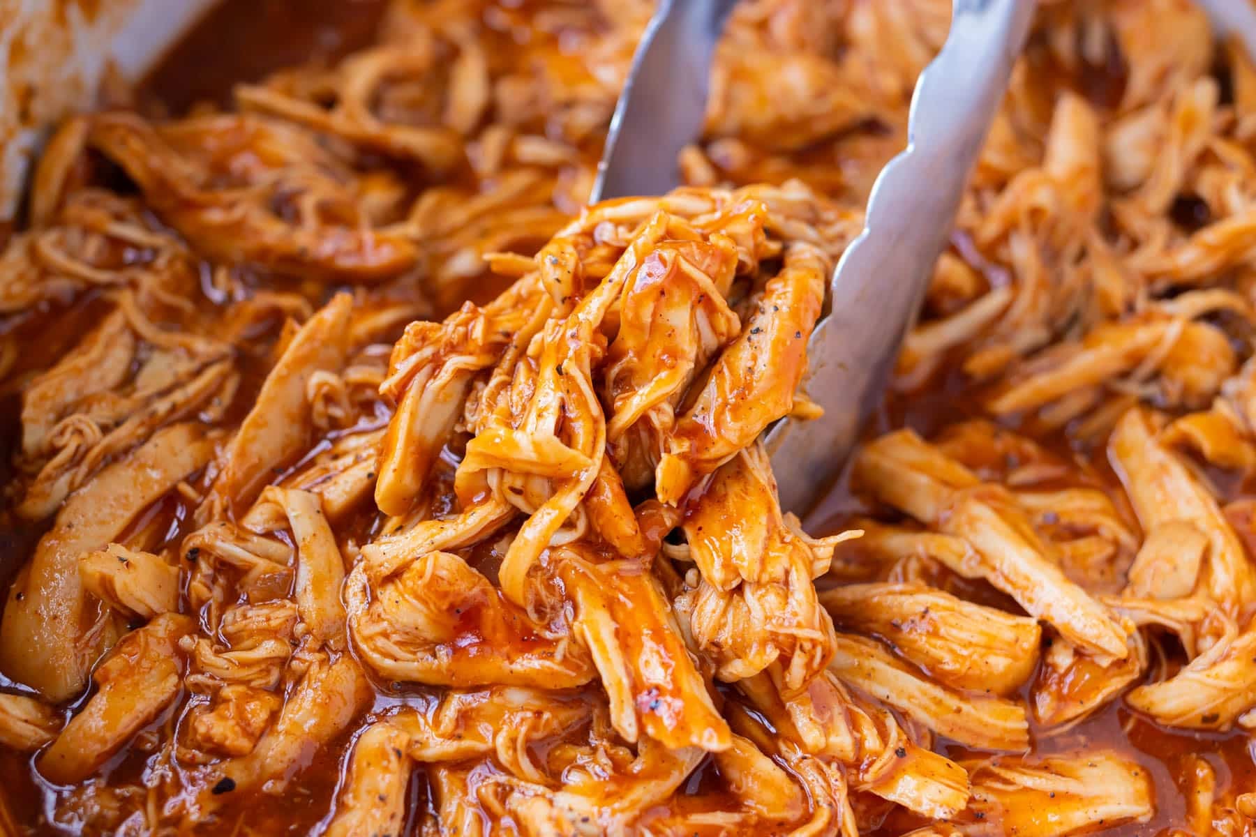 Two forks shredding cooked Slow Cooker BBQ Shredded Chicken right in the slow cooker.