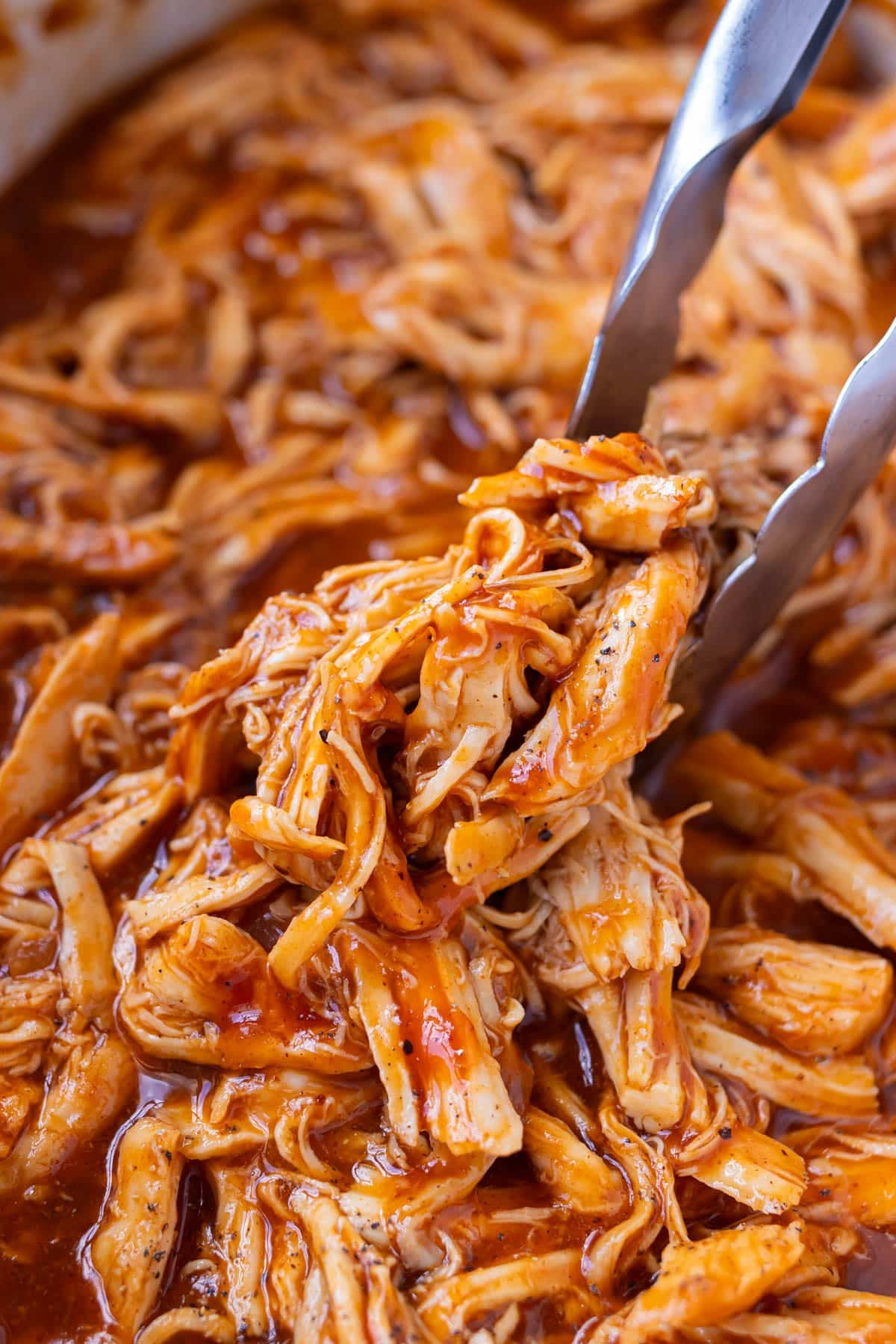 Slow cooker bbq shredded chicken being picked up from a Crock-Pot with tongs.