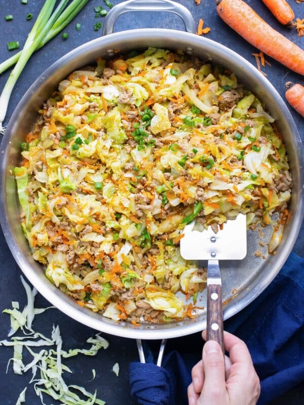 A low-carb and keto egg roll in a bowl recipe is being scooped out of a skillet with a spatula.