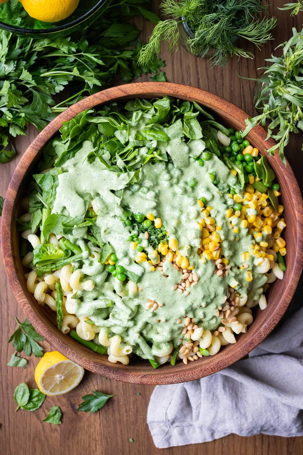 Green goddess dressing is poured over pasta, peas, corn, and spinach for a summer pasta salad recipe.