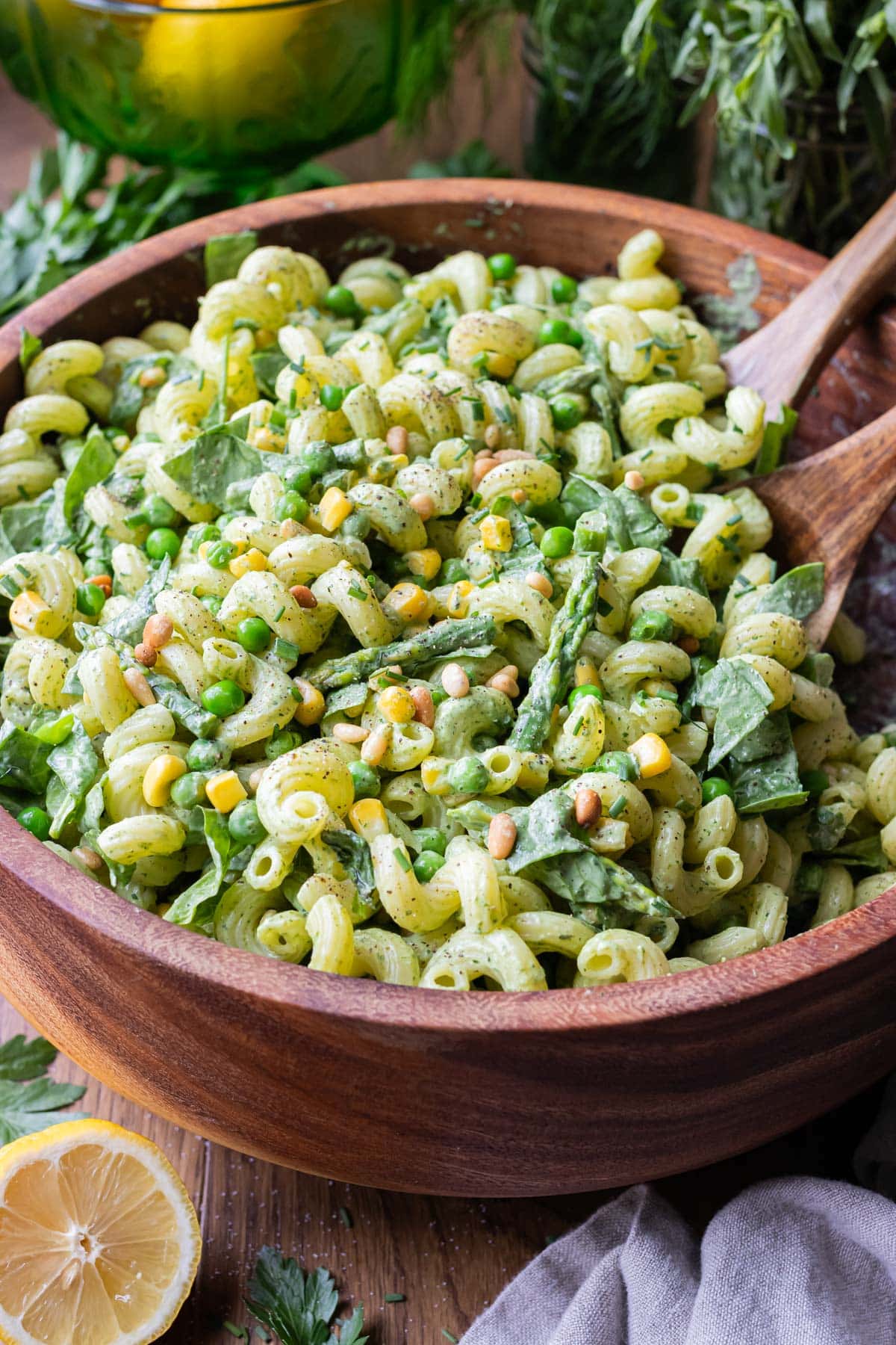 A wooden salad bowl is full of a pasta salad with green goddess dressing.