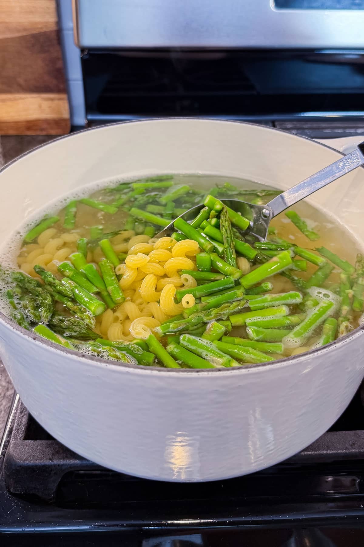 Pasta and asparagus are being scooped up out of a pot of boiling water.