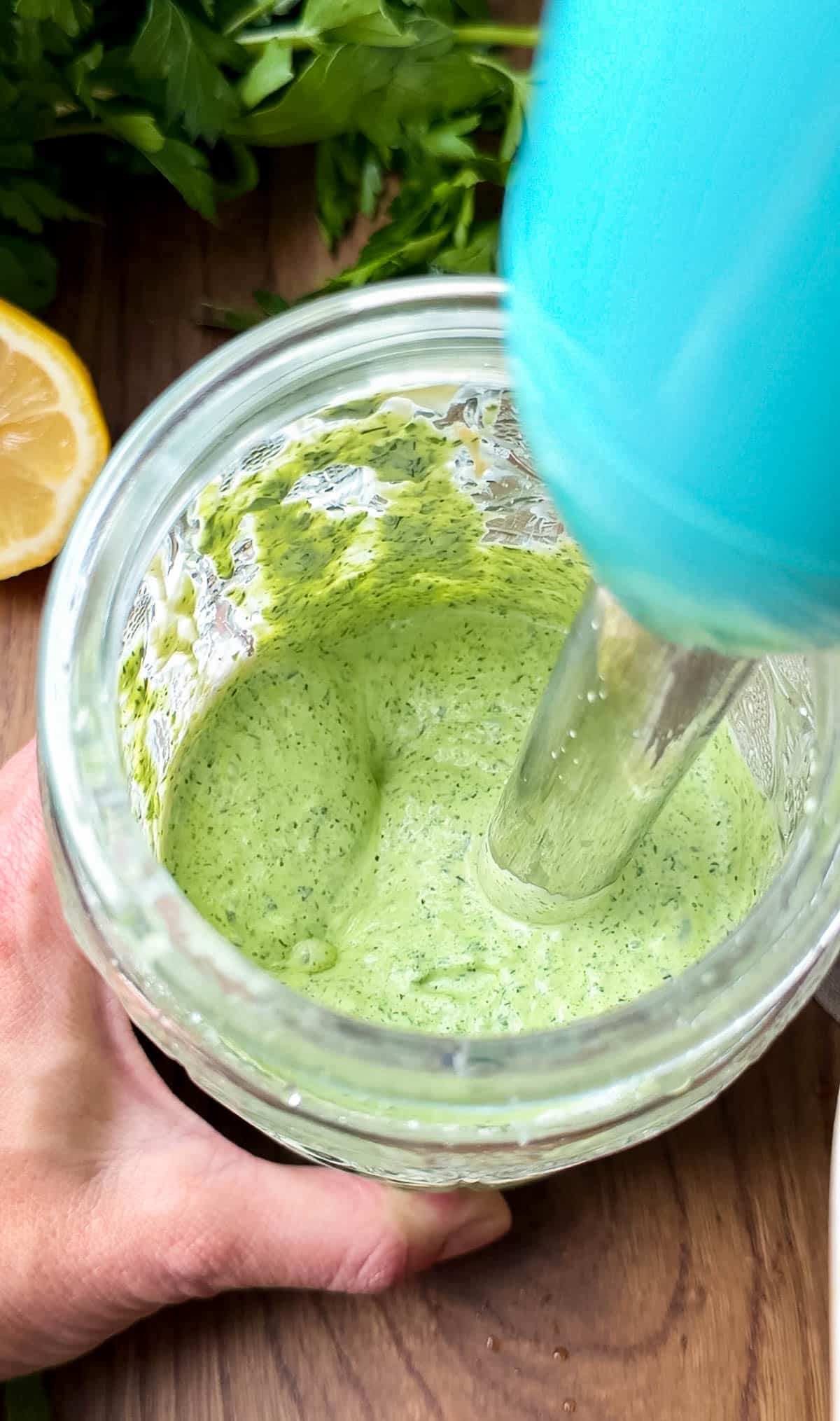 Green goddess dressing is blended in a jar using an immersion blender.
