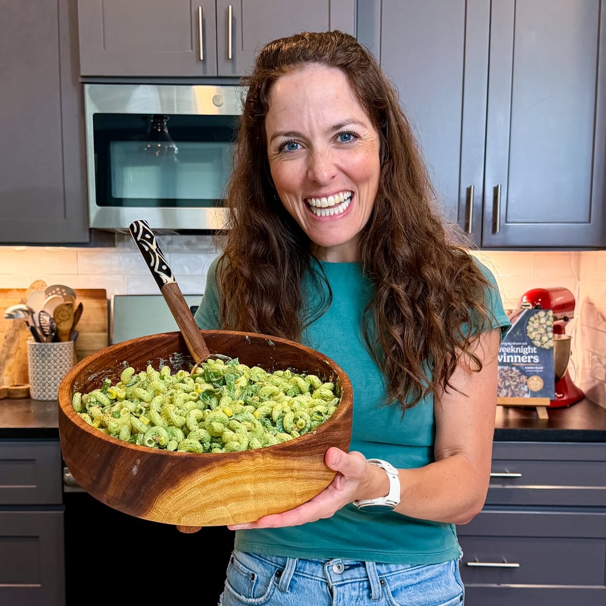 London Lea is holding a serving bowl full of a pasta salad with a green goddess dressing on it.