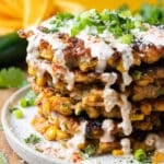 A stack of Mexican street corn fritters are on a plate with a chili lime crema sauce drizzled on top.