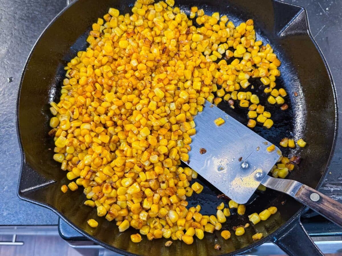 Corn getting charred in a cast iron skillet for a Mexican street corn fritters recipe.