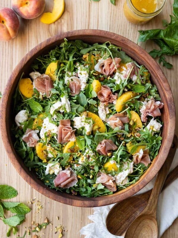 A Peach burrata salad with arugula and pistachios is served with a hot honey vinaigrette.