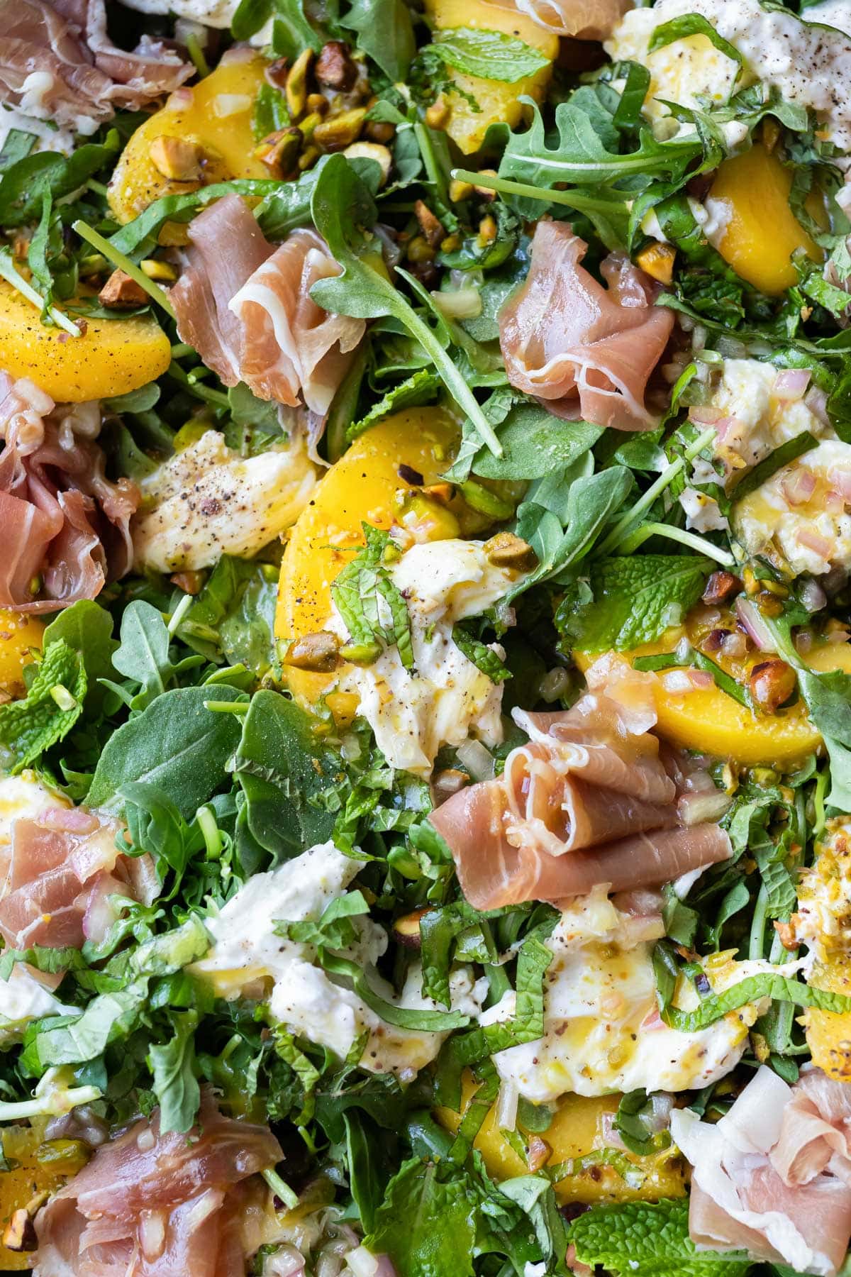 Close-up of peach burrata salad showing ripe peaches, creamy burrata, prosciutto, and a hot honey vinaigrette drizzled on top.