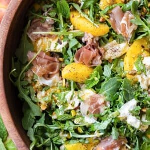 A Peach burrata salad with arugula and pistachios is served with a hot honey vinaigrette.