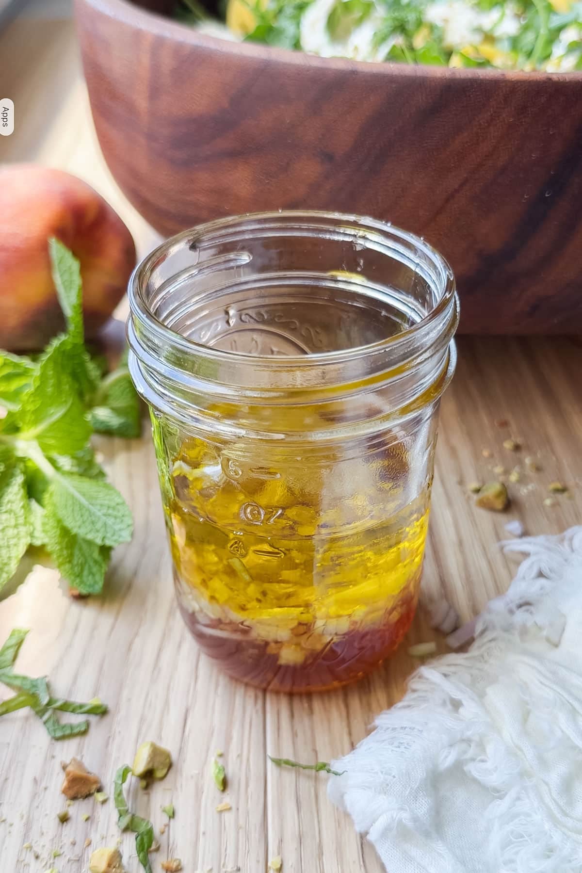 Hot honey vinaigrette in a small mason jar on a wooden surface with fresh mint and a peach.