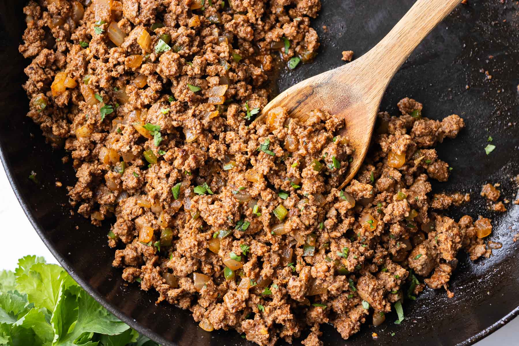 Close up of a wooden spoon scooping up some seasoned ground beef taco meat.
