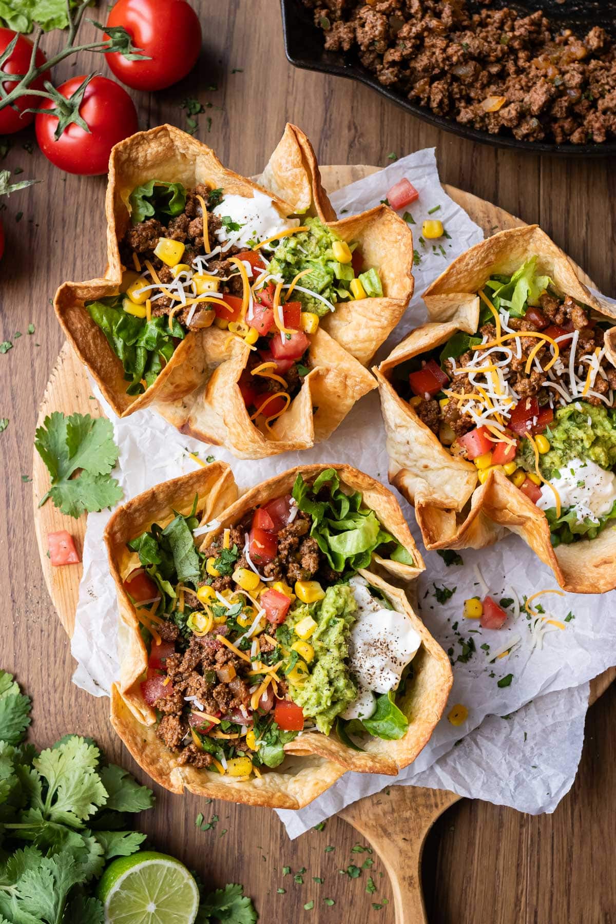 Three taco salad bowls are on a serving tray with a bubbly taco shell, seasoned ground beef taco meat, and tons of fresh topping.