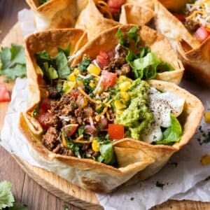 A taco salad bowl with a crispy and bubbly taco salad shell is filled with ground beef taco meat, cheese, tomatoes, and other fresh toppings for an easy dinner.