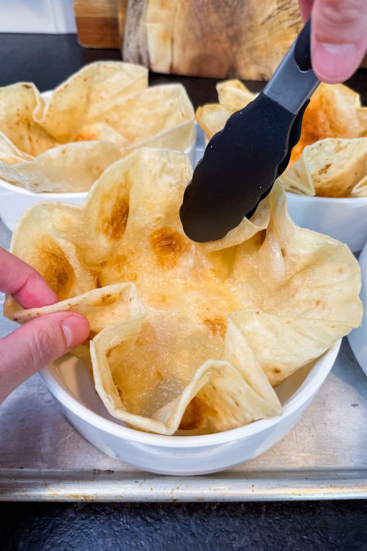 Tongs are used to place a hot oiled tortilla into pasta bowls before baking into taco salad shells.