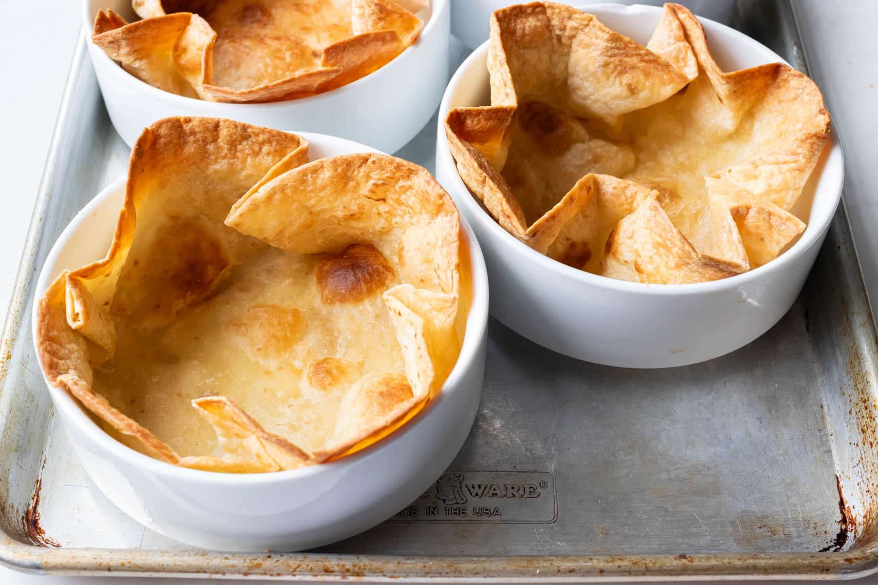 Crispy bubbly taco salad shells fresh from the oven on a sheet pan.