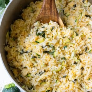 A pot of creamy zucchini rice being stirred with a wooden spoon