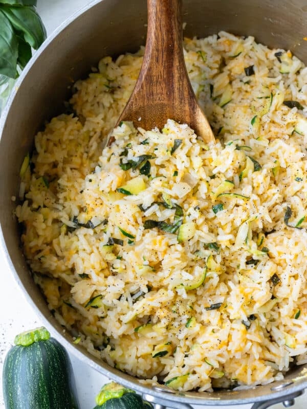 A pot of creamy zucchini rice being stirred with a wooden spoon