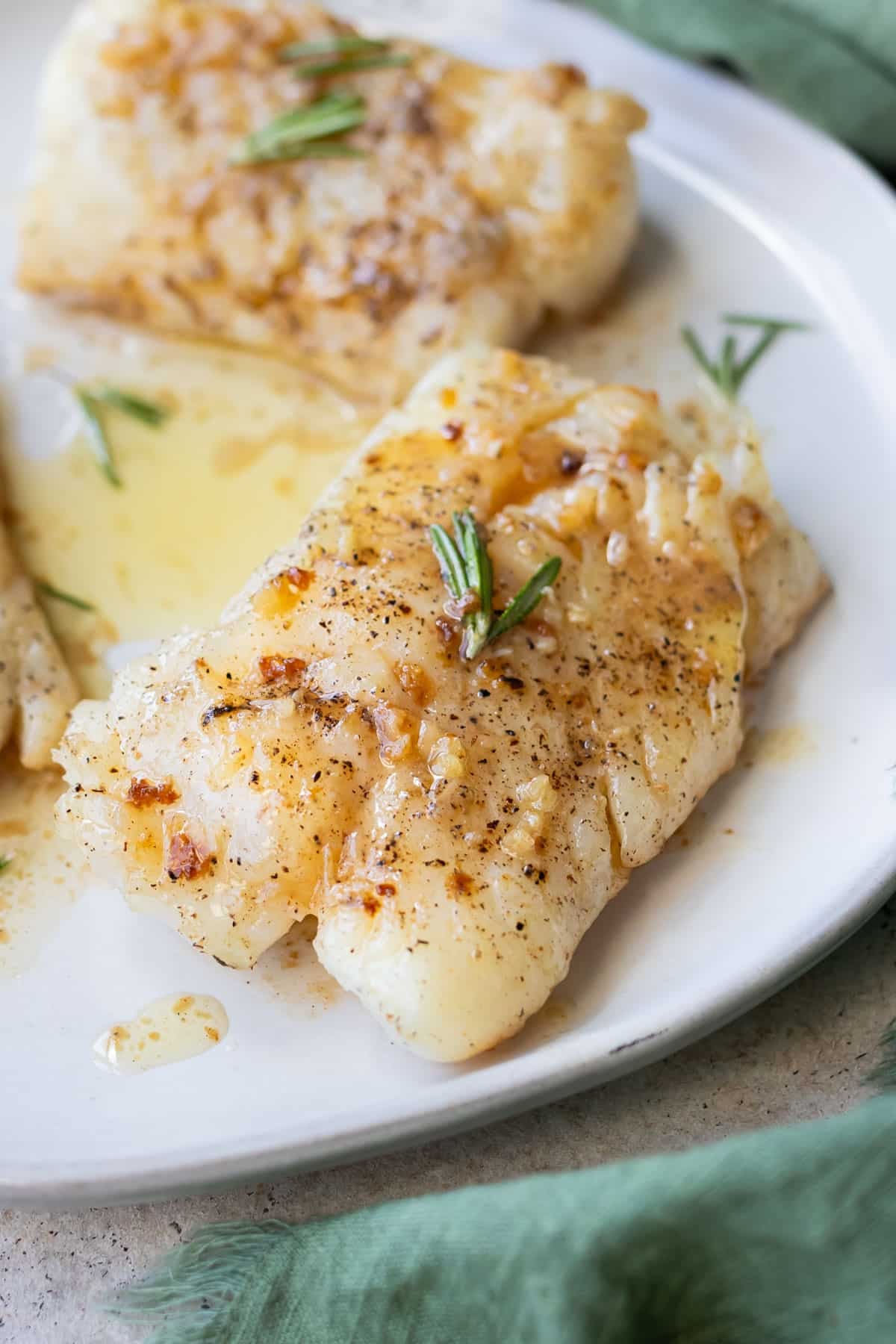 A plated garlic butter cod fillet flaked with a fork.