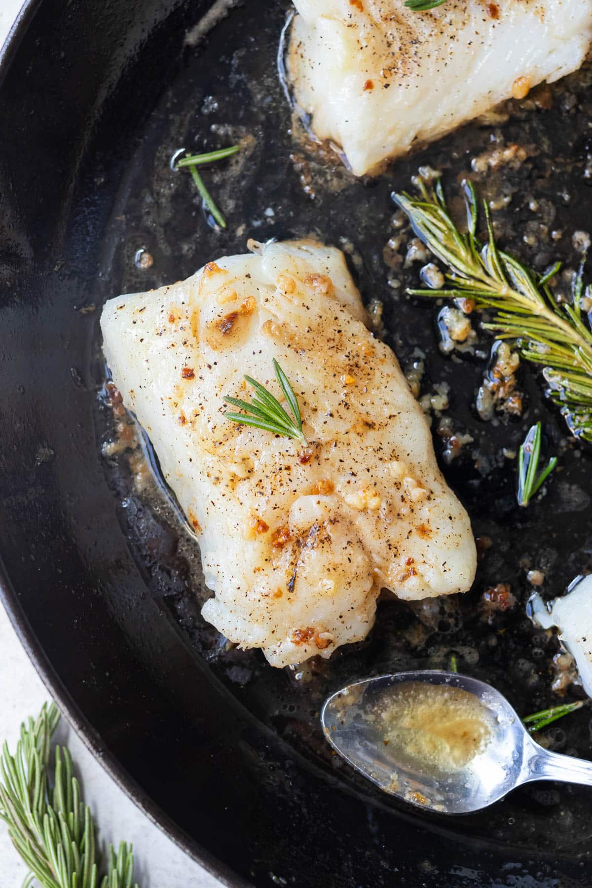 Pan seared garlic butter cod with rosemary in a cast iron skillet.
