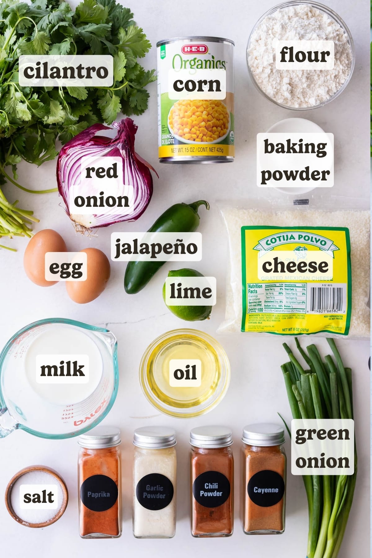 Corn, cilantro, jalapenos, milk, cotija cheese, baking powder, flour, and spices are the ingredients for Mexican street corn fritters on a table.
