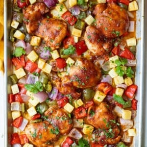 A sheet pan Hawaiian Chicken dinner is pulled out of the oven with caramelized chicken thighs, bell peppers, and pineapple.
