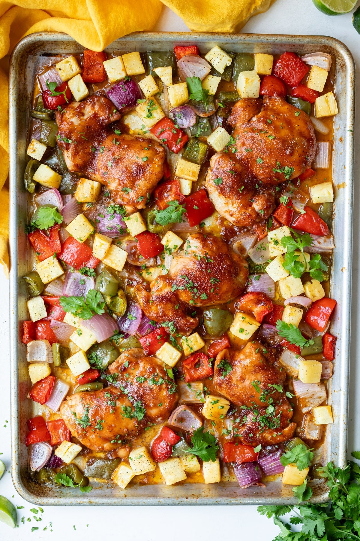 A sheet pan Hawaiian Chicken dinner is pulled out of the oven with caramelized chicken thighs and pineapple.