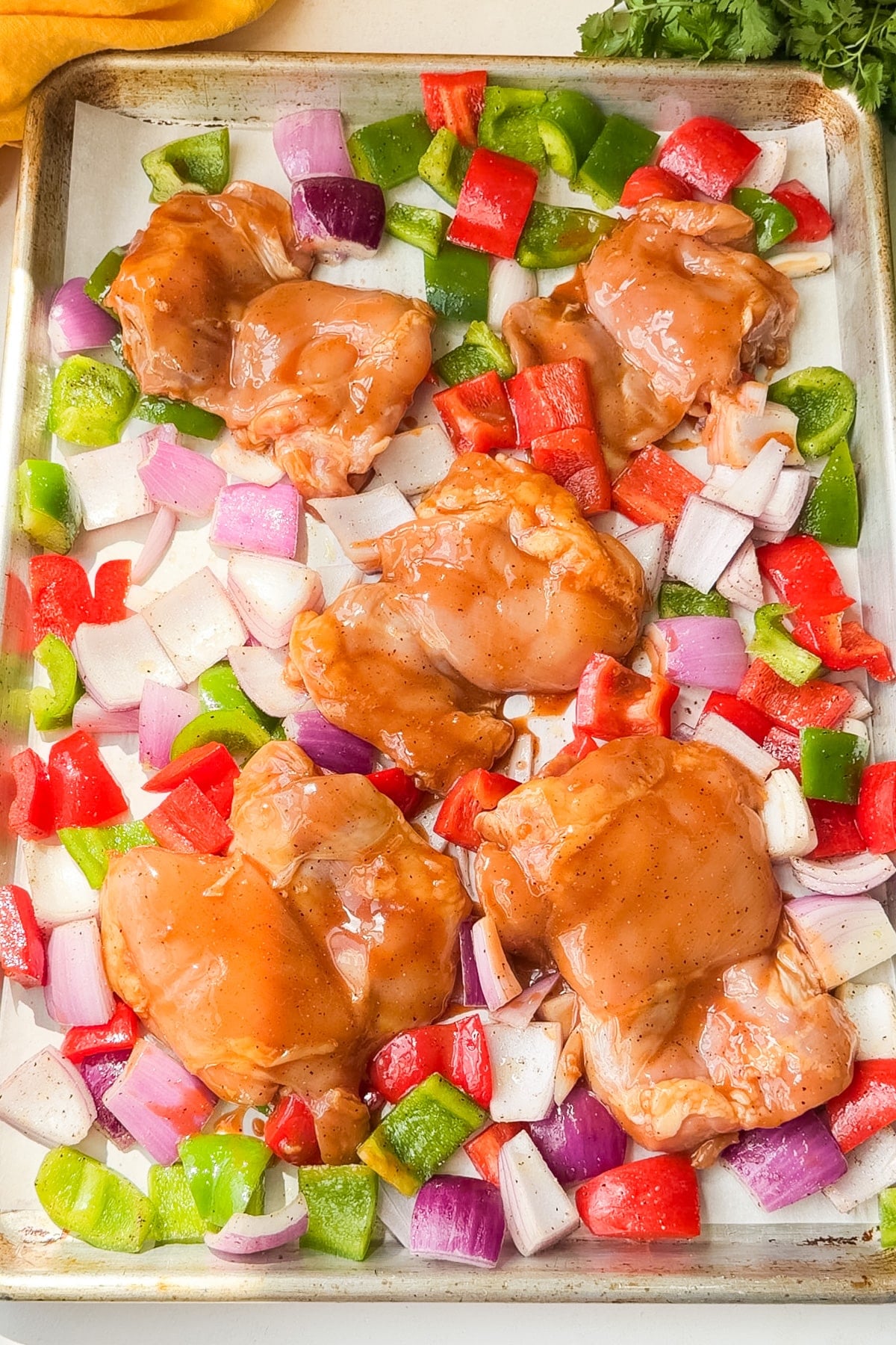 Marinated chicken thighs and vegetables spread in a single layer on a sheet pan of Hawaiian chicken.