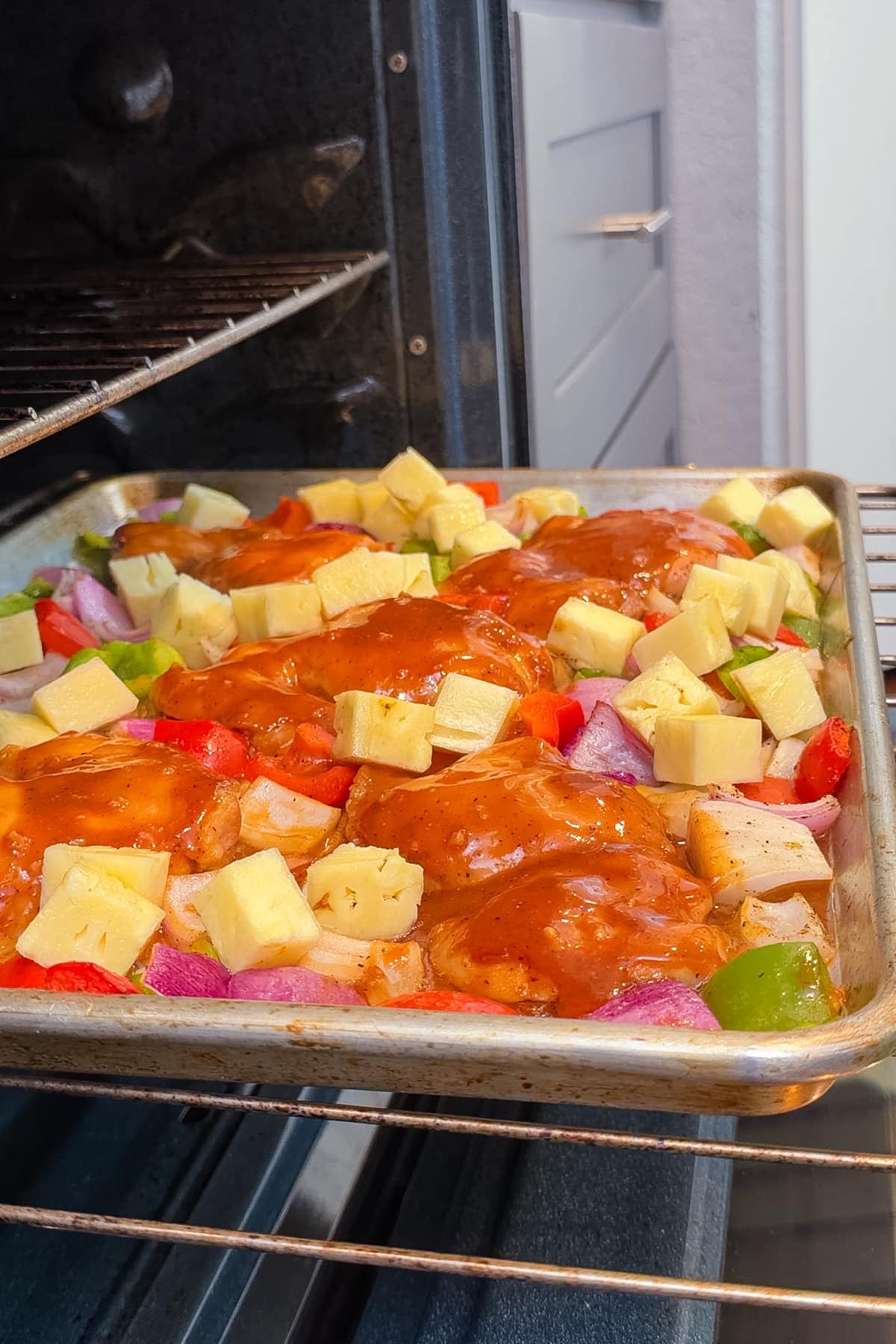 Chicken thighs, pineapple, and bell peppers are on a sheet pan in the oven for a Hawaiian-style recipe.