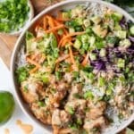 Overhead view of a Bang Bang Chicken Bowl with crispy chicken, rice, carrots, cucumber, and red cabbage next to a small bowl of bang bang sauce.